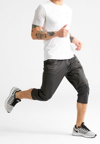 Camiseta blanca de manga corta con acentos texturizados, pantalones cortos deportivos negros y zapatillas gris con detalles en negro y blanco, en una pose de carrera.