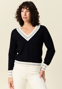 Pull tricot marine à col en V, avec des accents côtelés blancs et gris au niveau du col et des poignets ; design ajusté, texture douce.