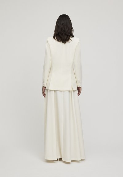 Blazer bianco su misura e gonna lunga, caratterizzati da un tessuto morbido, un design strutturato e dettagli con bottoni sui polsini della giacca.