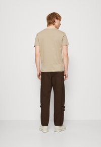 Tricou bej din bumbac, asociat cu pantaloni cargo maro, dotati cu fermoare laterale si mansete elastice, completat cu adidași de culoare deschisă.