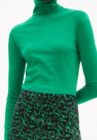 Grön långärmad polotröja i ett mjukt tyg, kombinerad med en strukturerad svart kjol med ett grönt abstrakt mönster.