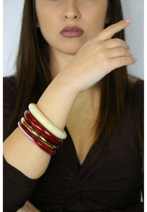 Cztery bransoletki na nadgarstku: dwie czerwone, jedna beżowa, jedna ze złotymi akcentami. Gładkie, błyszczące wykończenie; różne szerokości i kolory.
