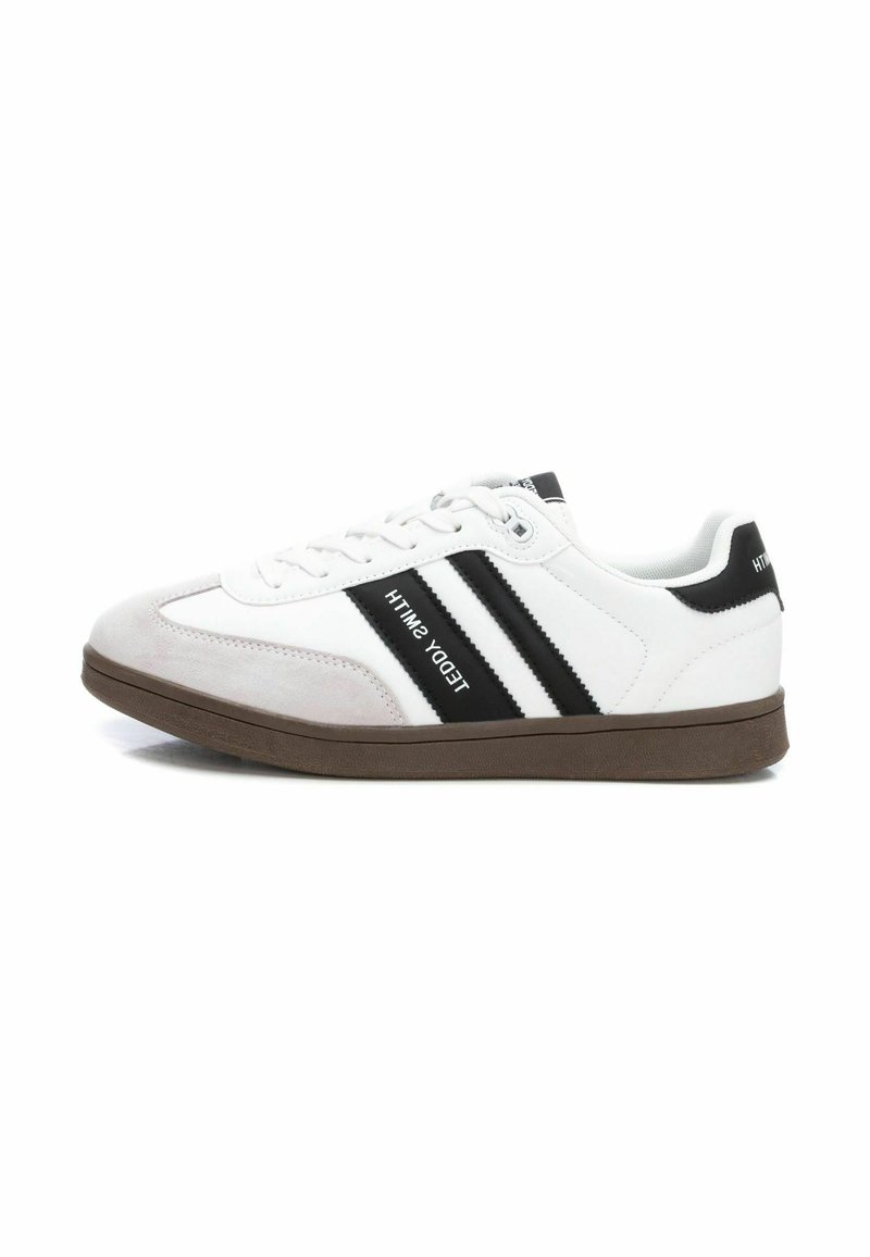 Zapatillas blancas con rayas negras, puntera de ante y suela de goma marrón. Presentan una marca en el lado y un diseño de cordones.
