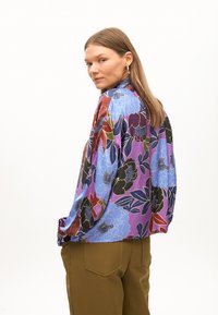 Blusa floreale colorata in tonalità di viola, blu e rosso; tessuto setoso, maniche lunghe, vestibilità ampia e dettagli delle maniche arricciate.