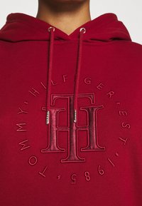 Czerwona bluza z kapturem z podniesionym, haftowanym logotypem Tommy Hilfiger oraz teksturowanymi sznurkami z metalowymi końcówkami. Miękki, bawełniany materiał.