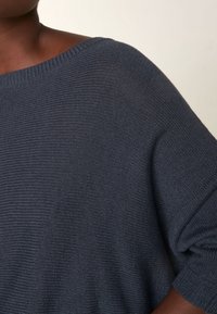 Ciemnoniebieski sweter dziany o luźnym kroju, szerokim dekolcie i teksturowanej tkaninie z subtelnym połyskiem. Rękawy wykończone ściągaczami dopełniają design.