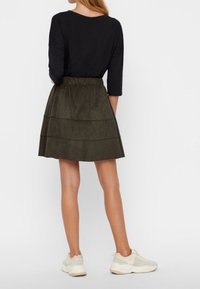 Tmavý top s dlouhým rukávem v kombinaci s vícestupňovou sukní z olivově zeleného semiše; bílé tenisky celý outfit doplňují.