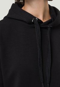 Zwarte hoodie met een gladde textuur, voorzien van een capuchon met trekkoord, platte gevlochten koorden en metalen aglets voor accenten.