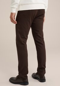 Pantaloni subțiri de culoare maro, dintr-un material neted, având un talie mijlocie și picioare drepte, asortați cu pantofi slip-on de culoare închisă.