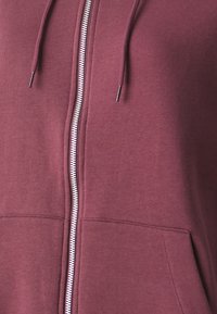 Felpa zip-up color bordeaux con una cerniera argento, lacci e due tasche frontali, realizzata in morbido tessuto a maglia.