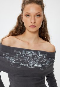 Schulterfreies, geripptes Oberteil in Dunkelgrau mit weißem Grafikdruck "State of Mind." Langärmlig mit taillierter Passform.