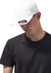 Hvid kasket med en buet skygge, prydet med et sort klistermærke på skyggen, båret af en person i en sort t-shirt. Blødt stof, tætsiddende design.