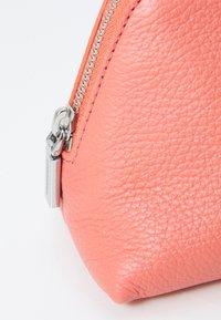 Pochette in pelle corallo con finitura testurizzata, chiusura con zip argentata e dettagli brandizzati sulla linguetta della zip. Forma triangolare.