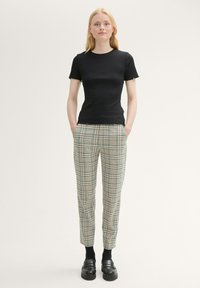 Black ribbed short-sleeve top with frayed edges paired with green and beige plaid trousers, featuring side pockets, slim fit, and black loafers.