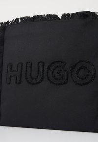 Crna platnena torba s teksturiranim, izvezenim logotipom "HUGO". Torba ima resasti rub i glatku površinu s minimalističkim dizajnom.