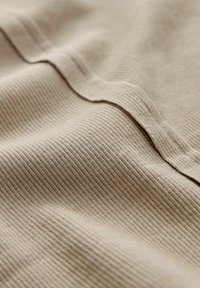 Beige, gerippter Stoff mit einer strukturierten Oberfläche, der einen subtilen Glanz aufweist. Das Material zeigt feine horizontale Linien und sanfte Falten.