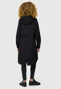 Abrigo negro impermeable con capucha, que presenta un diseño corto en la parte delantera, mangas largas y una abertura en la parte trasera para ventilación.