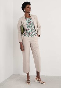 Bežna obleka s krojenimi hlačami in bluzo s cvetličnim potiskom. Dopolnjena z zelenim nahrbtnikom in belimi blok-peta sandalami.