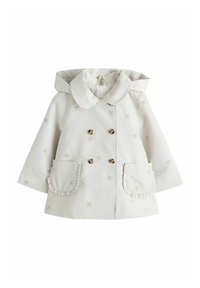 Valge vihmamantel, millel on suur krae, topeltreestriga kullavärviliste nööpidega, volangidega taskuservad ja kogu pinnal väikeste lipsude tikandid.