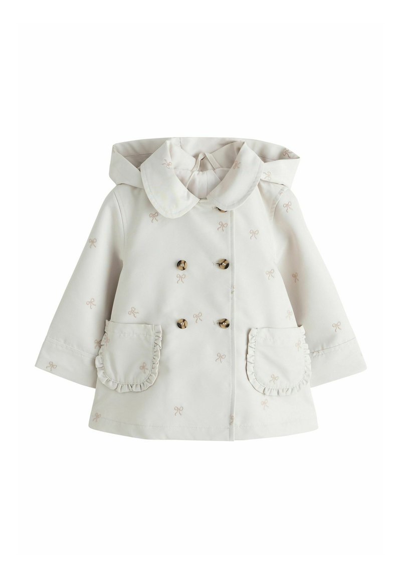 Valge vihmamantel, millel on suur krae, topeltreestriga kullavärviliste nööpidega, volangidega taskuservad ja kogu pinnal väikeste lipsude tikandid.