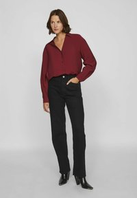 Camisa burdeos de botones con cuello, combinada con jeans negros de pierna recta y botas negras de tobillo. La camisa tiene una tela texturizada.