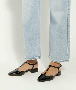 Zwarte patenten leren schoenen met lage hak, een T-band ontwerp, spitse neus en gouden hardware accent, gedragen met lichtblauwe high-waisted jeans.