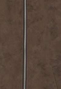 Veste en faux cuir marron avec une fermeture éclair argentée centrale, surface texturée, et une poche latérale avec des lignes épurées et sans ornements visibles.