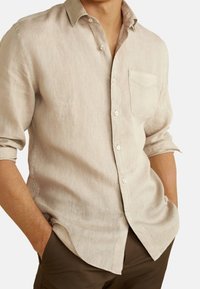 Chemise beige en lin à boutons avec col, poche poitrine unique et manches retroussées, présentant un tissu texturé et léger.