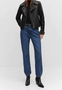 Veste en cuir synthétique noire avec un col gris, assortie à un jean droit bleu et des bottes à talons noires. Texture lisse et design élégant.