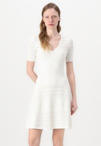 White dress with short, textured lace sleeves and a V-neck. Features a varied knit pattern on the body and flared skirt.