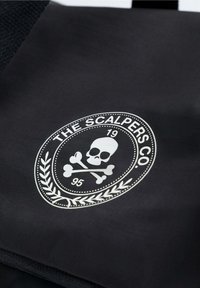 Bolsa de tela negra con un logo circular que presenta una calavera con huesos cruzados, rodeado por un diseño de laurel y el texto "THE SCALPERS CO."