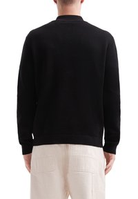 Pull en maille noir avec une texture côtelée, manches longues et col montant. Présente un ourlet droit et un minimum de détails à l'arrière.