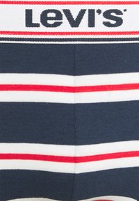 Tasca a righe blu di Levi's con strisce orizzontali rosse e bianche, caratterizzata da un logo nero prominente nella parte superiore. Texture a maglia liscia.