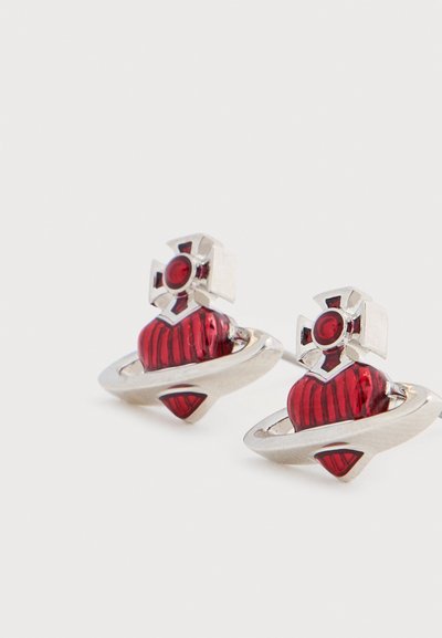 Σκουλαρίκια σε ασημί απόχρωση με κόκκινο μενταγιόν σε σχήμα καρδιάς, περιβαλλόμενο από ένα δαχτυλίδι και επάνω διακοσμημένο με σταυρό, με λαμπερό φινίρισμα και περίτεχνες λεπτομέρειες.