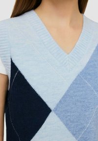 Gilet lavorato a maglia blu chiaro con scollo a V, caratterizzato da un motivo a rombi in blu scuro e blu chiaro. Texture liscia e colletto a costine.