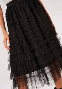 Jupe en tulle noir à plusieurs couches avec un design à volants, dotée d'une taille élastique et de longueurs de volants variées pour ajouter de la texture et du mouvement.