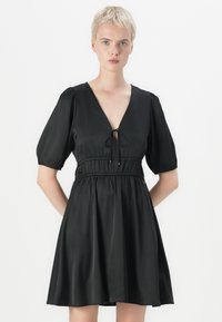 Vestido preto com um decote em V profundo, mangas bufantes e uma cintura elástica. Feito de um tecido suave, alarga suavemente a partir da cintura.