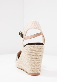 Sandalo con zeppa dotato di una fascia intrecciata beige e dettagli in tessuto nero, presentante una piattaforma in espadrille texturizzata e una fibbia alla caviglia regolabile.