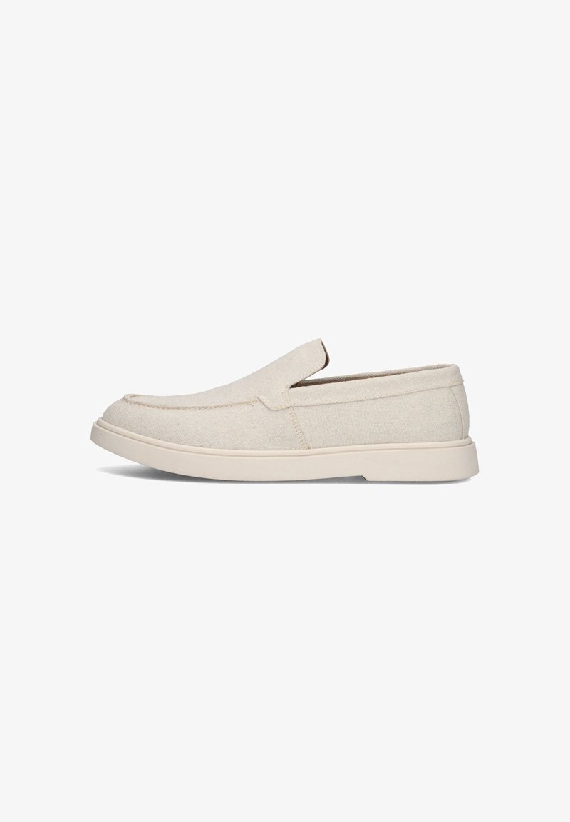 Beige instappers met een bovenwerk van canvas en een witte rubberen zool, getoond in profiel op een witte achtergrond.