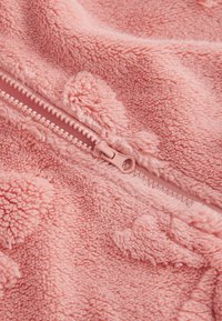 Rosa fleece tyg med en mjuk, texturerad yta, med en dragkedja som har en matchande rosa dragring. Mönstren liknar små hjärtan.