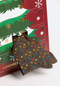 Brown socks with colorful polka dots emerging from a green and red advent calendar featuring a Christmas tree design.
