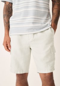 Light green cargo shorts made of textured fabric with side pockets. The shorts have a relaxed fit and a simple hemline.