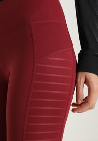 Bordowe legginsy sportowe z gładką fakturą, siateczkowym panelem bocznym z poziomymi paskami oraz wysokim stanem.