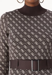 Pull en tricot marron avec un motif ivoire complexe, col montant côtelé et ceinture en tissu ornée d'une boucle rectangulaire.