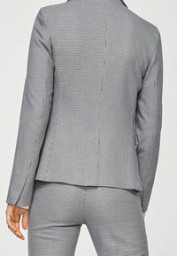 Blazer grigio a quadri con vestibilità sagomata, dotato di colletto con revers a incavo, spacco posteriore e motivo in tessuto texturizzato. Abbinato a pantaloni coordinati.
