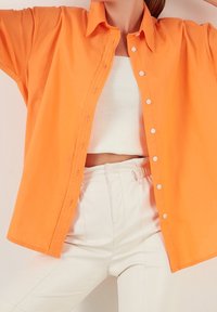 Orange knäppskjorta med avslappnad passform, långa ärmar och vita knappar, kombinerad med vita byxor med hög midja.