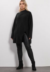 Czarny, oversize sweter z dzianiny z kołnierzem, z boku z rozcięciem i teksturowanym materiałem. Połączony z czarnymi skórzanymi legginsami i botkami za kostkę.