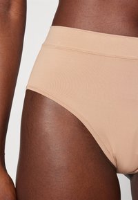 Beige gaćice visokog struka, izrađene od glatkog materijala s bešavnim dizajnom. Imaju ravnu traku u struku i prilagođene su za udobnost.