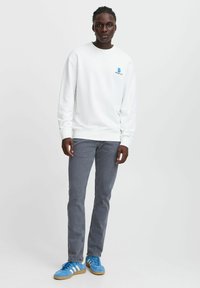 Sudadera blanca con un logo azul, pantalones vaqueros ajustados grises y zapatillas azules. Tejido suave con puños y dobladillo acanalados. Diseño simple.