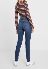 Jeans ajustados de talle alto en color azul, con un diseño de cinco bolsillos y un ligero estiramiento. Combinados con una camiseta de rayas de manga larga y zapatillas blancas.